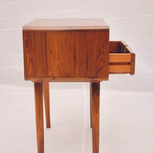 May include: A wooden end table with a single drawer that is open. The table has four legs and is made of a dark wood.