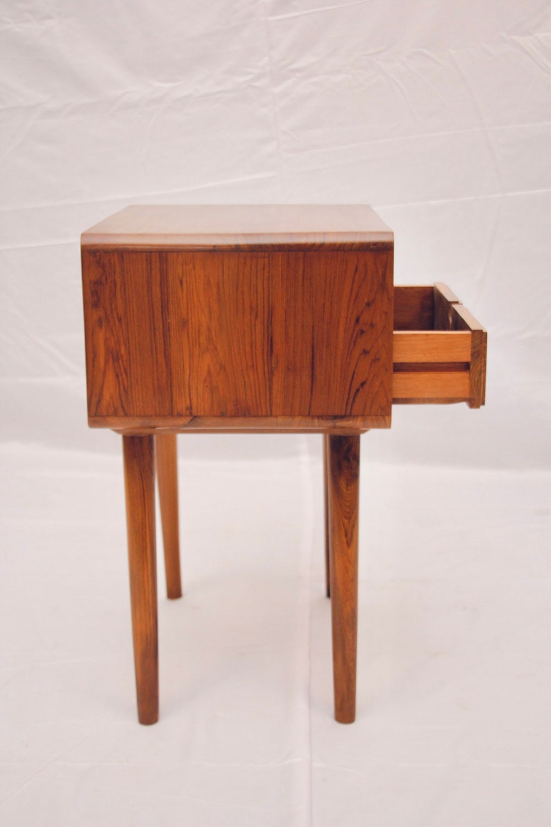 May include: A wooden end table with a single drawer that is open. The table has four legs and is made of a dark wood.