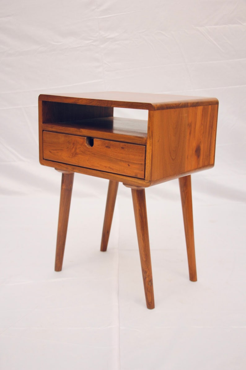 May include: A wooden end table with a single drawer and a shelf. The table has four tapered legs and a light brown finish.