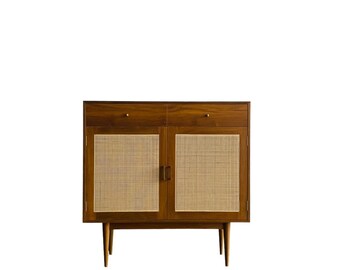 May include: A mid-century modern cabinet with two doors and two drawers. The doors are made of woven cane and the cabinet is finished in a rich brown wood.