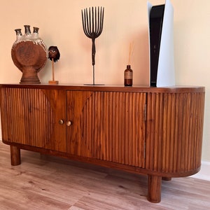 May include: A dark wood cabinet with two doors and a curved top. The cabinet has a ribbed design and brass hardware. The cabinet is sitting on a light wood floor.