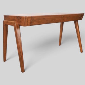 May include: A mid-century modern wooden desk with a rectangular top and four angled legs. The desk is made of a warm-toned wood and features a drawer. The desk is approximately 48 inches long.