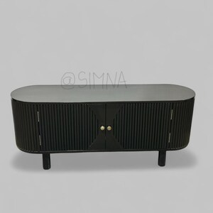 May include: Black oval-shaped cabinet with two doors and gold knobs. The doors have vertical grooves and the cabinet sits on four short legs.