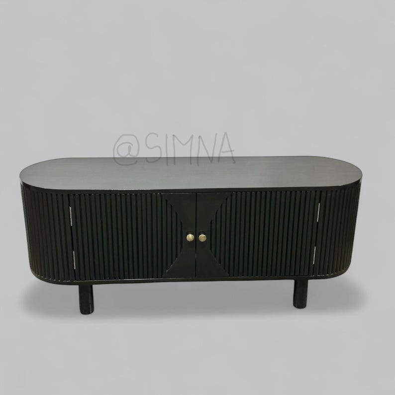 May include: Black oval-shaped cabinet with two doors and gold knobs. The doors have vertical grooves and the cabinet sits on four short legs.