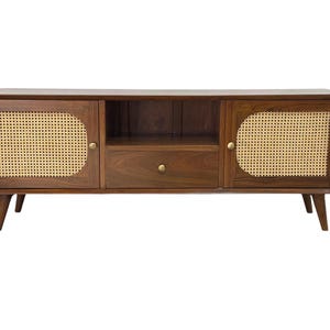 May include: A dark brown wooden TV stand with two doors and a drawer. The doors have woven cane panels and brass knobs. The stand has four legs.