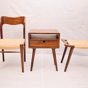 May include: A set of three wooden furniture pieces: a chair, a side table with a drawer, and a stool. All three pieces have a natural wood finish and woven cane seats.