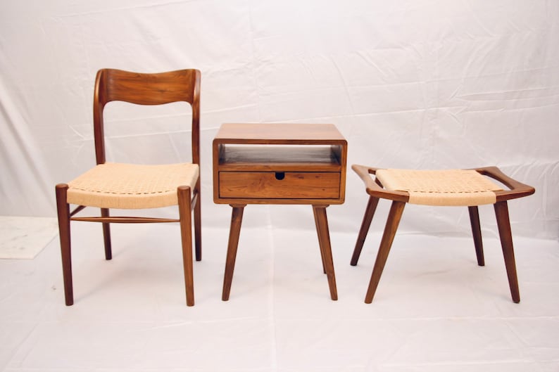 May include: A set of three wooden furniture pieces: a chair, a side table with a drawer, and a stool. All three pieces have a natural wood finish and woven cane seats.