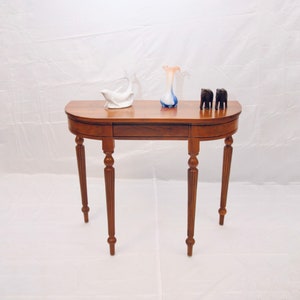 Könnte beinhalten: Ein halbrunden Holztisch mit gedrehten Beinen und einer glatten, dunkelbraunen Oberfläche. Der Tisch ist mit einer weißen Porzellanfischfigur, einer blauen und weißen Glasvase und zwei kleinen schwarzen Holzelefanten dekoriert.