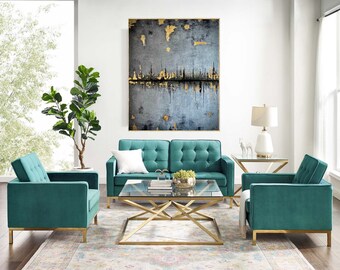 Puede incluir: Una sala de estar con un sofá de terciopelo azul verdoso y dos sillones a juego. El sofá y los sillones tienen patas doradas. Una mesa de centro de vidrio con un marco de metal dorado se encuentra frente al sofá. Un gran cuadro abstracto cuelga de la pared detrás del sofá.