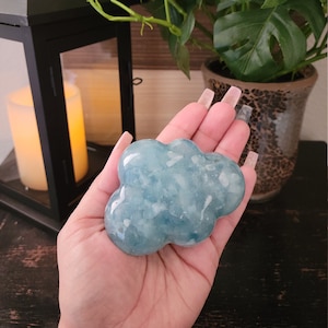 May include: A light blue, cloud-shaped crystal with white inclusions. The crystal is smooth and polished.