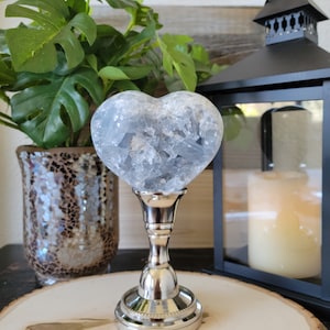 May include: A heart-shaped crystal cluster on a silver stand. The crystal is clear with a light blue hue and has a rough, natural texture.