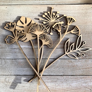 May include: A set of five wooden laser cut floral shapes, including a monstera leaf, a ginkgo leaf, a flower, and two different types of sprigs. The shapes are all natural wood colour and have a rustic, farmhouse style.