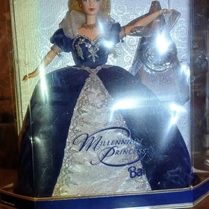 May include: A blue and silver Barbie doll in a box. The doll is wearing a blue and silver gown with a crown. The box says "Special Millennium Edition" and "Millennium Princess Barbie".