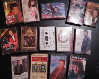 May include: A selection of vintage cassette tapes, featuring country music artists. The tapes display album covers with portraits of musicians such as Vince Gill, Jim Reeves, and Patty Loveless. Titles include "Let There Be Peace On Earth" and "Wrangler Cowboy Christmas."
