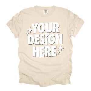 May include: A beige t-shirt with the text "YOUR DESIGN HERE" in white. The text is stylized with a heart and stars.