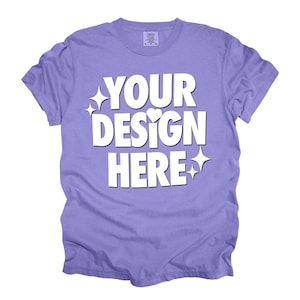 May include: A purple t-shirt with the text "YOUR DESIGN HERE" in white. The text is stylized with sparkles and a heart.