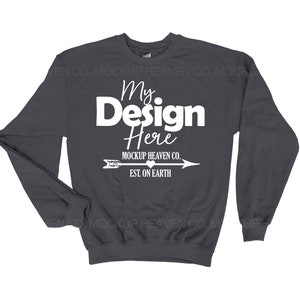 Könnte beinhalten: Ein dunkelgrauer Pullover mit langen Ärmeln und einem Rundhalsausschnitt. Die Vorderseite des Pullovers trägt den Text "My Design Here" in Weiß, mit einem kleinen Herzen und einem Pfeil darunter. Der Text "MOCKUP HEAVEN CO. EST. ON EARTH" ist ebenfalls in Weiß unter dem Pfeil gedruckt.