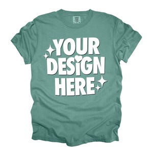 May include: A teal blue t-shirt with the text "YOUR DESIGN HERE" in white. The text is stylized with a heart and stars.
