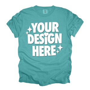 May include: A turquoise blue t-shirt with the text "YOUR DESIGN HERE" in white. The text is stylized with a heart and sparkles.