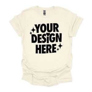 Puede incluir: Una camiseta de color crema con mangas cortas y cuello redondo. La camiseta tiene el texto "YOUR DESIGN HERE" impreso en negro en la parte delantera.