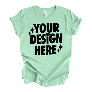 May include: A light green t-shirt with the text "YOUR DESIGN HERE" in black lettering. The text is surrounded by small black stars and a heart.