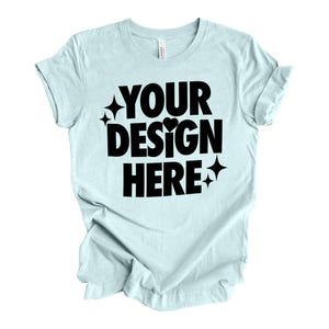 May include: A light blue t-shirt with the text "YOUR DESIGN HERE" in black. The text is in a bold, playful font with a small heart and stars.