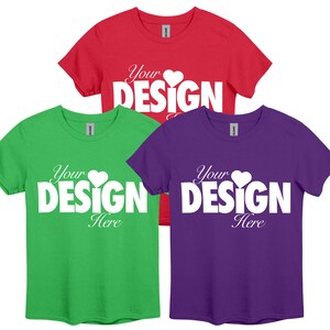 May include: Three t-shirts in different colours: red, green, and purple. Each shirt has the text "Your DESIGN Here" printed in white with a small heart symbol.