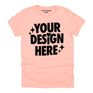 May include: A peach-colored t-shirt with the text "YOUR DESIGN HERE" in black. The text is surrounded by small stars and hearts.
