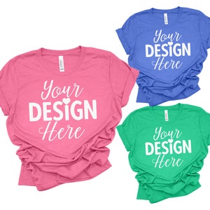 May include: Three t-shirts in different colors: pink, blue, and green. Each shirt has the text "Your Design Here" printed on the front in white with a small heart symbol.