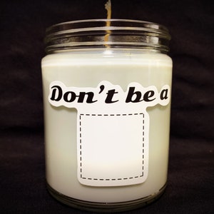 May include: A white candle in a glass jar with a white label that says "Don't be a" with a blank space for text.
