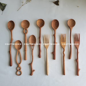 Puede incluir: Un conjunto de cucharas y tenedores de madera con mangos únicos con forma de rama. Las cucharas y los tenedores están hechos de madera natural y tienen un aspecto rústico y artesanal. Los mangos son todos de diferentes formas y tamaños, lo que aumenta el carácter único de cada pieza.