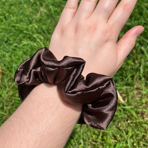 May include: A brown satin scrunchie, a hair tie, worn on a person's wrist.