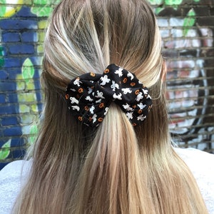 Op de afbeelding: Een zwarte haarband met een witte en oranje Halloween-print met geesten en pompoenen.