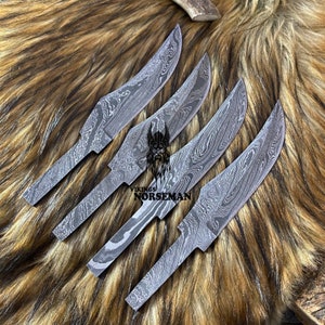 Peut inclure: Quatre lames de couteau en acier Damas avec un motif de lignes ondulées. Les lames sont disposées en éventail sur une surface en fourrure brune. Le texte "Vikings Norseman" est visible sur les lames.