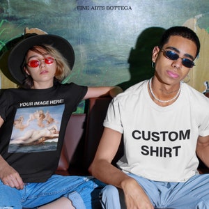 May include: Two people wearing custom t-shirts. The person on the left is wearing a black t-shirt with a painting of a woman and angels. The person on the right is wearing a white t-shirt with the text "CUSTOM SHIRT" in black.