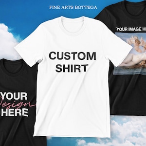 May include: Three t-shirts, one white, one black, and one black with a painting of a woman and two angels. The white t-shirt has the text "CUSTOM SHIRT" printed on it. The black t-shirt has the text "YOUR DESIGN HERE" printed on it. The black t-shirt with the painting has the text "YOUR IMAGE HERE!" printed on it.