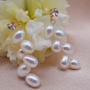 May include: A pair of gold earrings with a single clear rhinestone and a dangling cluster of white pearls.