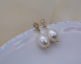 May include: A pair of gold earrings with a white pearl and a clear crystal drop. The earrings are on a white plate.