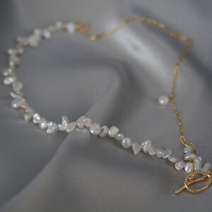 May include: A delicate gold chain necklace with a clasp closure. The necklace is adorned with small, irregular white pearl-like beads.