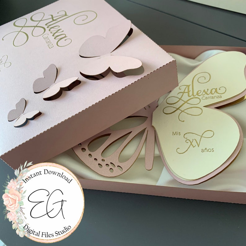 May include: A pink box with a butterfly design and the name "Alexa Carranza" on the top. The box is open and inside is a white card with the same name and the text "Mis XV a&ntilde;os".