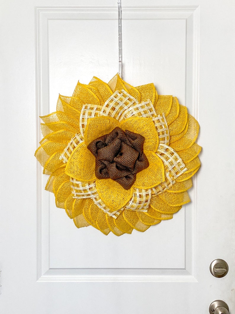 May include: A yellow sunflower wreath with a brown burlap center. The wreath is made of burlap and mesh and is perfect for a front door.