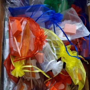 May include: A collection of small, colorful organza bags filled with various nail care items. The bags are in shades of red, orange, yellow, blue, green, white, and brown. The contents include orange nail buffers and wooden sticks.