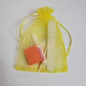 May include: A yellow organza drawstring bag containing nail care tools. The bag holds a nail file, a small orange buffer, a wooden cuticle stick, and a tube of nail glue. The nail glue tube has the text "KDS NAIL GLUE".