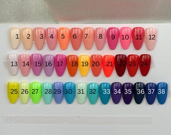 May include: A display of 38 artificial nails in various colors, arranged in rows. The colors range from light pastels to vibrant hues, including pinks, oranges, reds, purples, blues, and greens. Each nail is numbered for easy selection.