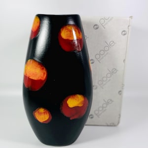 May include: A black ceramic vase with a speckled orange and red design. The vase is oval shaped and has a narrow opening. The vase is sitting on a white surface.