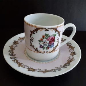 May include: A white porcelain teacup and saucer set with a pink rim and gold floral design. The cup has a handle and the saucer has a scalloped edge.