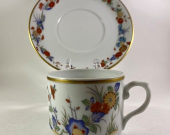 May include: A white porcelain teacup and saucer set with a gold rim and floral pattern in shades of blue, red, and yellow.