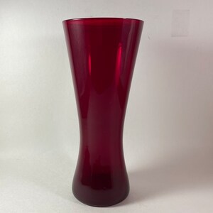 May include: A tall, slender, red glass vase with a rounded base.