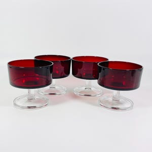 May include: Set of four red glass dessert dishes with clear glass stems. The dishes are round and have a slight lip.