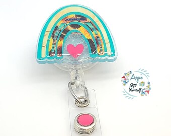 May include: A teal blue rainbow with a heart and sunflower pattern, a pink heart, and a clear retractable badge reel with a pink button.